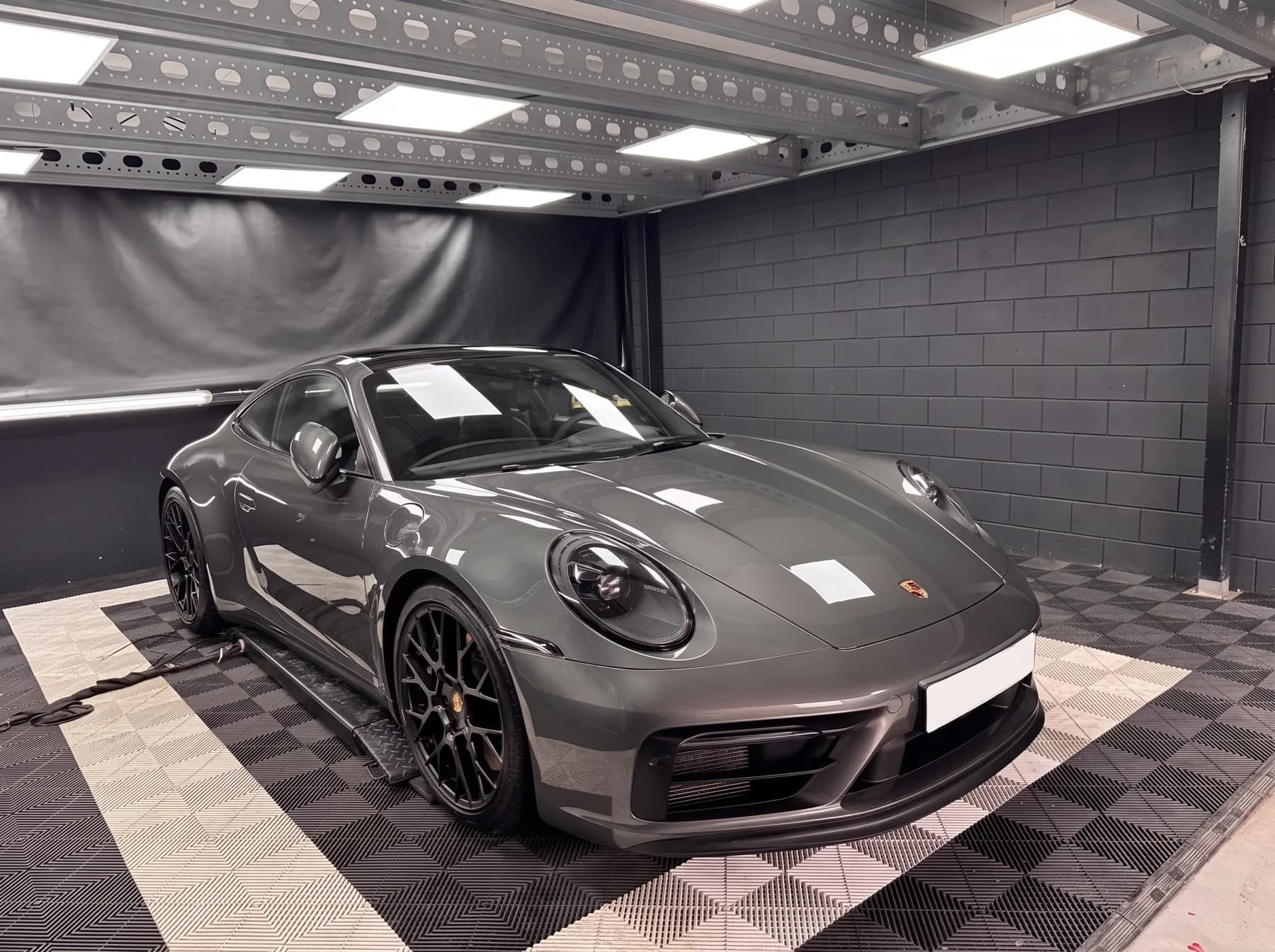 Grijze Porsche 911 na lakcorrectie, waarin de plafondverlichting als scherpe rechthoeken in de motorkap weerspiegelt