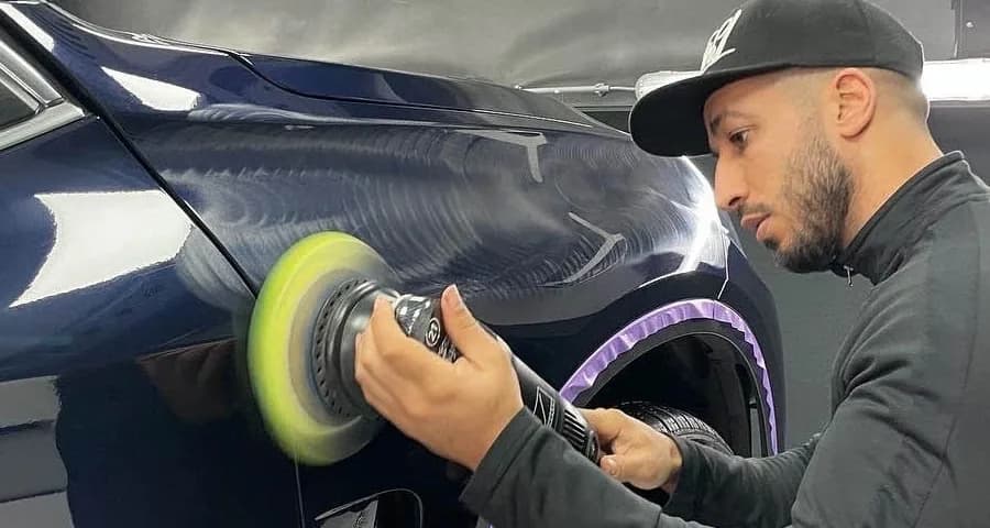 Detailer beweegt een polijstmachine over donkerblauwe lak waarin fijne cirkelvormige krassen zichtbaar zijn