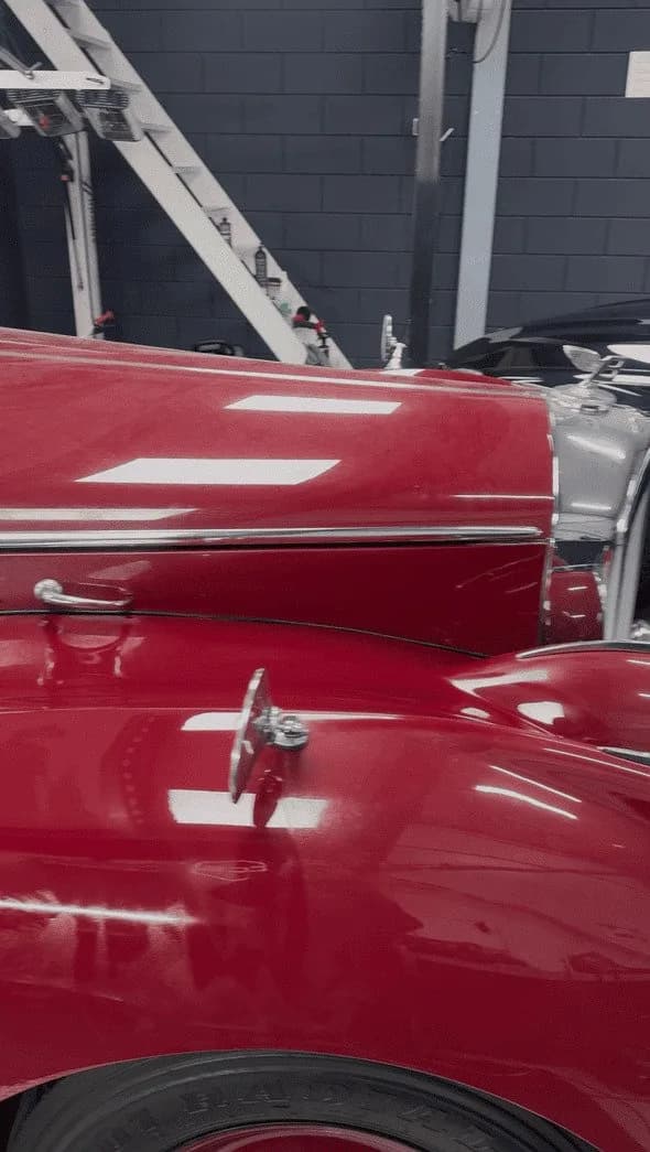 Detail van donkerrode Bentley-lak met fijne krassen en swirls onder werklicht