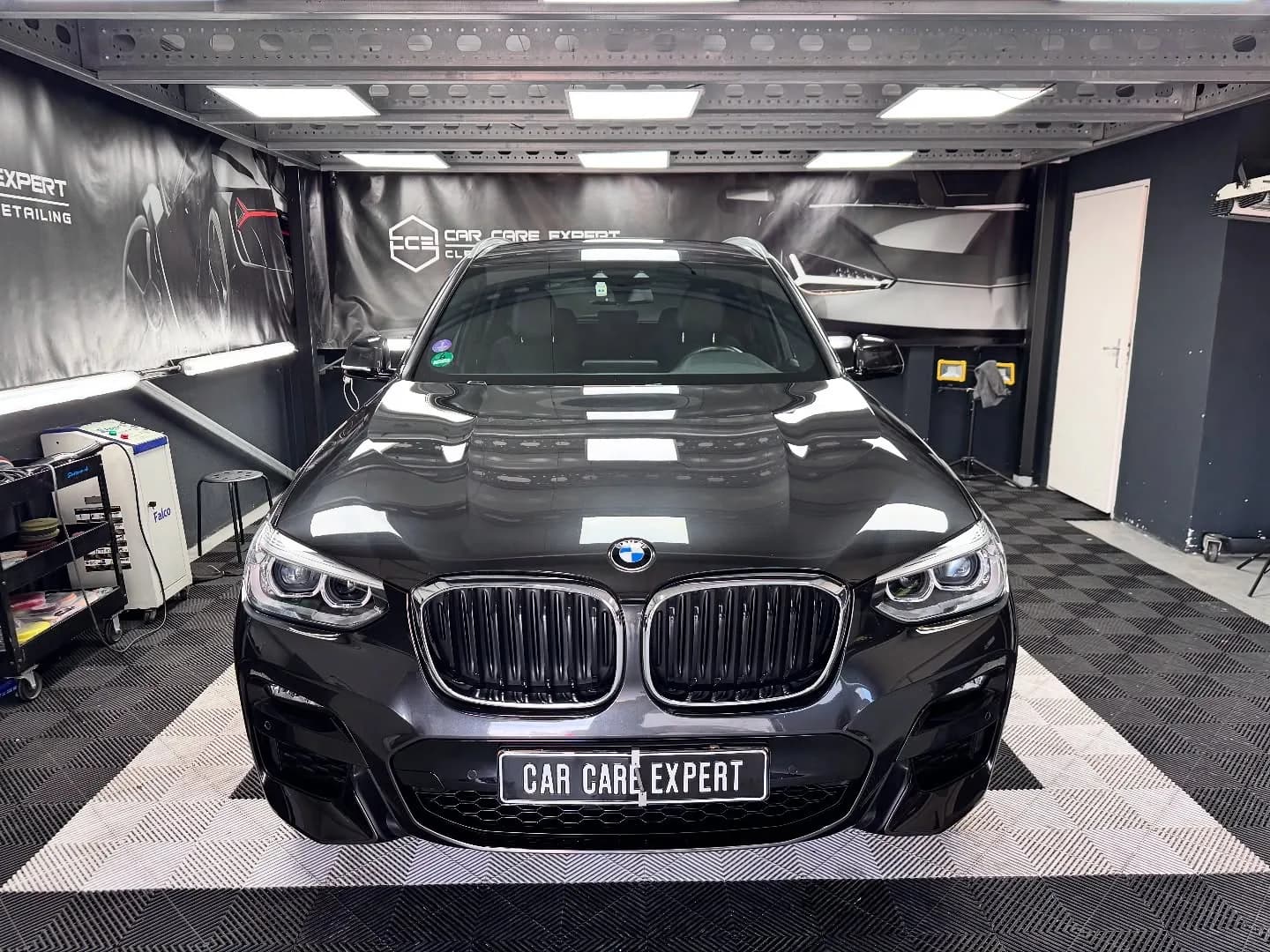 Zwarte BMW X3 recht van voren in de detailingstudio, met de plafondverlichting weerspiegeld in de motorkap