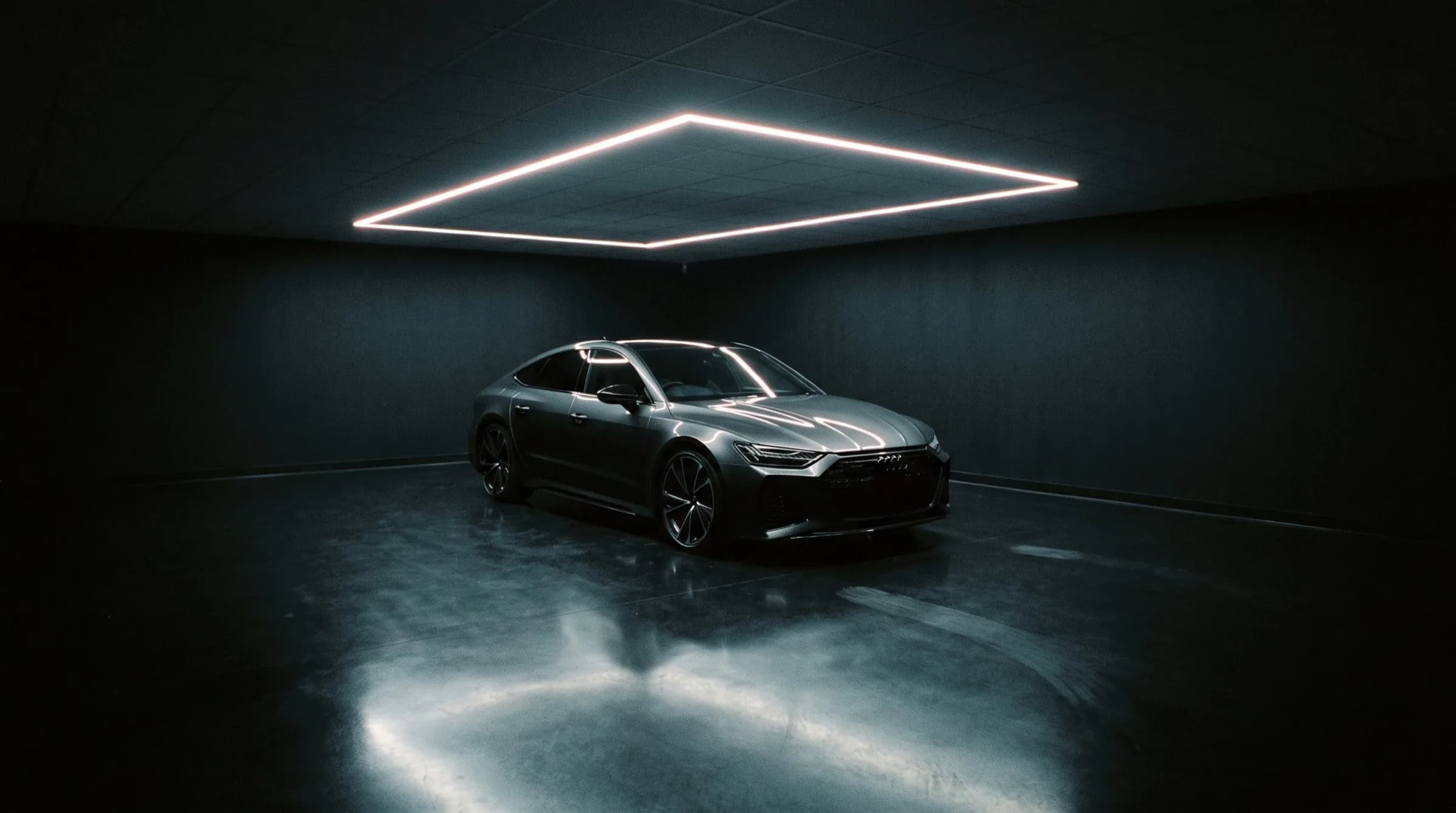 Donkere detailingstudio met een auto onder een lichtframe
