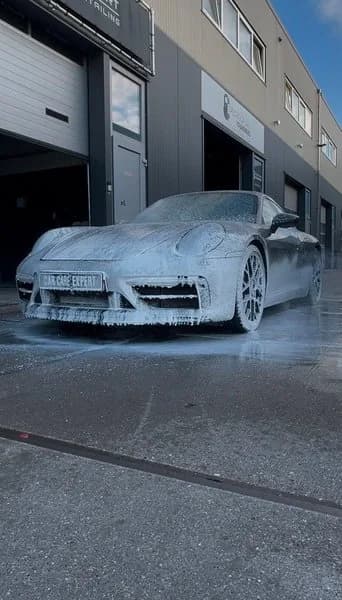 Donkergrijze Porsche 911 onder een laag schuim tijdens de voorwas
