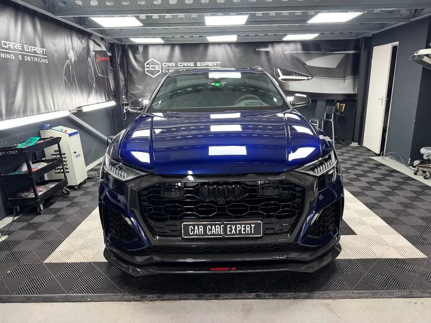 Donkerblauwe Audi RSQ8-S ABT recht van voren in de detailingstudio, met de plafondverlichting weerspiegeld in de motorkap